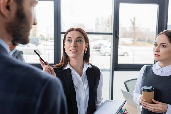 Businesswomen with notebook and coffee talking to blurred colleague — Stock Photo