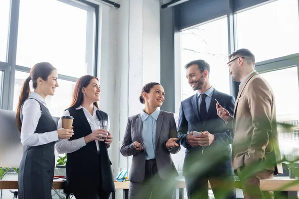 Femme d'affaires afro-américaine parlant à des hommes d'affaires souriants avec des boissons au bureau — Photo de stock