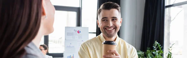 Homme d'affaires positif avec du café pour aller regarder collègue flou, bannière — Photo de stock