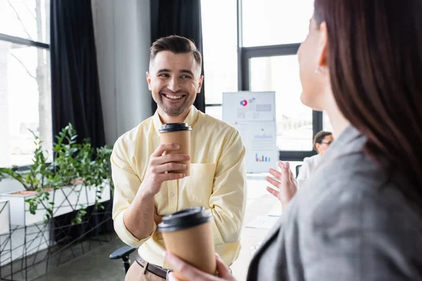 Позитивный бизнесмен держит кофе рядом с коллегой на размытом переднем плане в офисе — стоковое фото