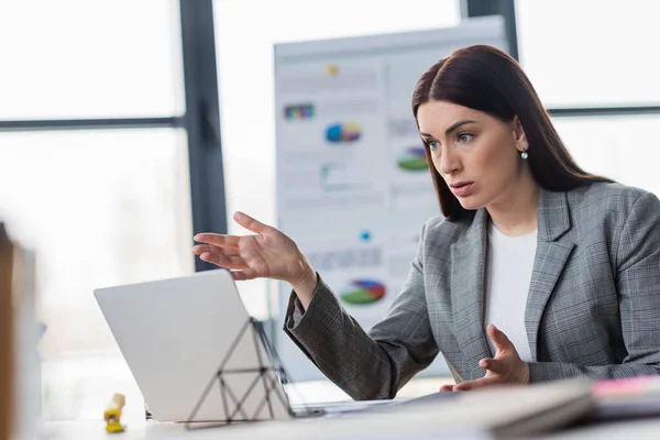 Femme d'affaires pointant avec la main pendant l'appel vidéo sur ordinateur portable dans le bureau — Photo de stock