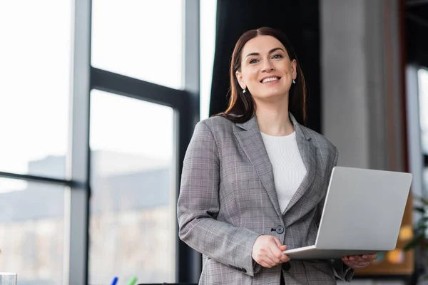 Businesswoman with laptop smiling at camera in office — Stock Photo