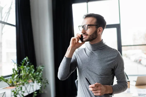 Empresario sosteniendo la pluma mientras habla en el teléfono inteligente en la oficina - foto de stock