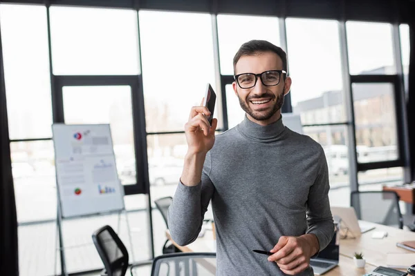Smiling manager in eyeglasses holding smartphone in office — Stock Photo