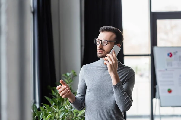 Менеджер в очках говорит на смартфоне рядом с заводом в офисе — стоковое фото
