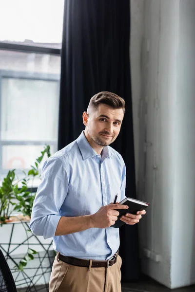 Homme d'affaires avec stylo et ordinateur portable regardant la caméra — Photo de stock