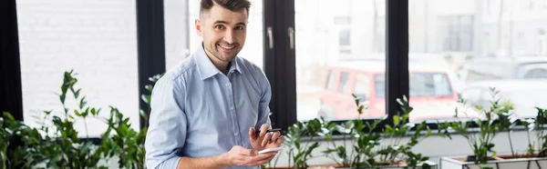 Homme d'affaires positif avec stylo tenant smartphone, bannière — Photo de stock