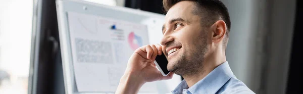 Gestionnaire parlant sur téléphone portable près de tableau à feuilles mobiles sur fond flou dans le bureau, bannière — Photo de stock