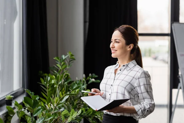 Mujer de negocios alegre con teléfono inteligente y portátil en la oficina - foto de stock