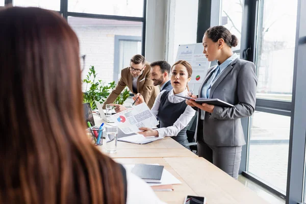 Geschäftsfrau zeigt multiethnischen Kollegen im Büro Dokument — Stockfoto