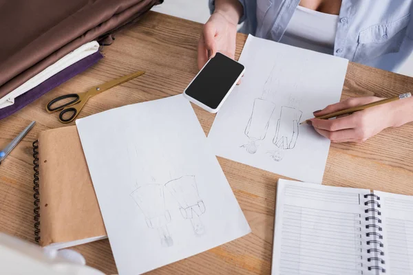 Vue recadrée de la couturière avec dessin smartphone près du tissu sur la table — Photo de stock