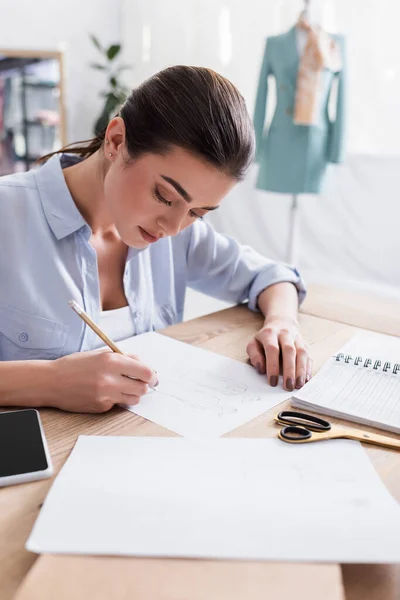 Seamstress drawing sketch near smartphone and scissors on table — Stock Photo