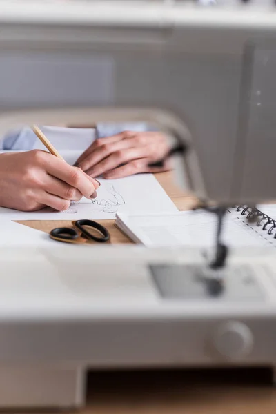 Cropped view of designer drawing sketch near blurred sewing machine — Stock Photo