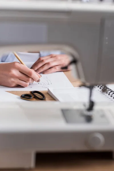 Vista recortada del dibujo del diseñador boceto cerca de la máquina de coser borrosa - foto de stock