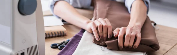 Vista recortada de costurera tomando tela cerca de tijeras y máquina de coser, pancarta - foto de stock