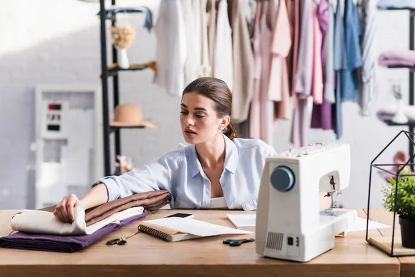 Couture regardant le tissu près du portable, smartphone et machine à coudre — Photo de stock