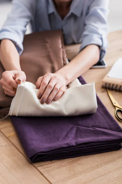 Cropped view of seamstress holding cloth near scissors on table — Stock Photo