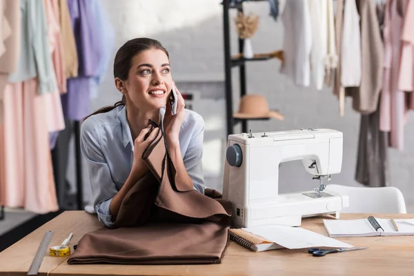 Seamstress talking on smartphone near cloth, ruler and sewing machine — Stock Photo