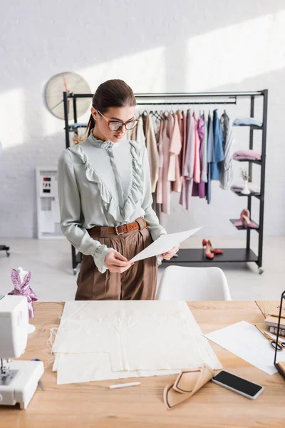 Designer hält Papier in der Nähe von Stoff und Nähmaschine — Stockfoto