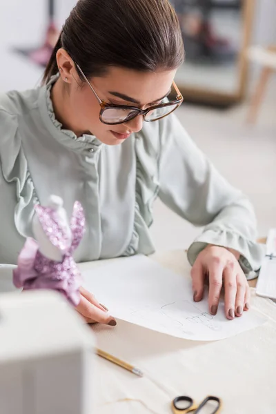 Designer looking at sketches near mannequin and cloth on blurred foreground — Stock Photo
