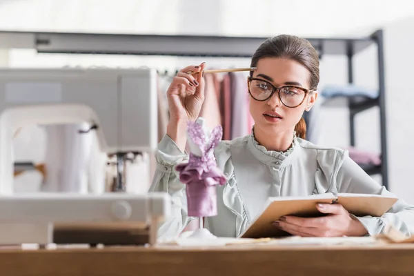 Designer hält Notizbuch und Bleistift neben Schaufensterpuppe auf verschwommenem Vordergrund — Stockfoto