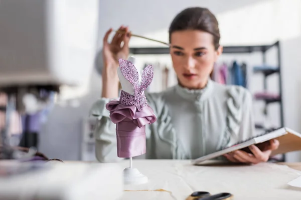 Schaufensterpuppe mit Kleid fast verschwommen Designer mit Notizbuch im Studio — Stockfoto