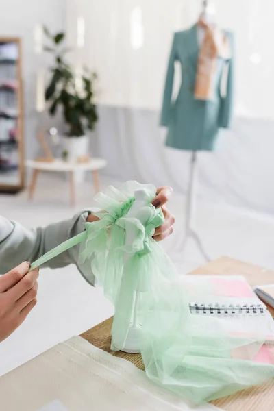 Cropped view of seamstress holding cloth and mannequin near blurred notebook on table — Stock Photo
