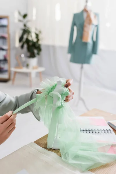 Vista recortada de costurera sosteniendo tela y maniquí cerca borrosa portátil en la mesa - foto de stock