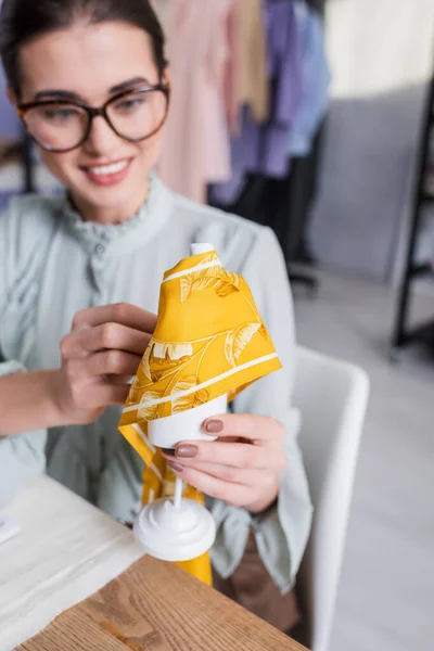 Tissu et mannequin dans les mains de couturière souriante sur fond flou — Photo de stock