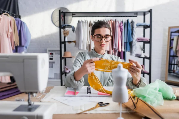 Seamstress holding cloth near blurred mannequin and sewing machine — Stock Photo