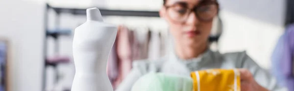 Maniquí cerca de costurera borrosa con tela sobre fondo borroso, bandera — Stock Photo