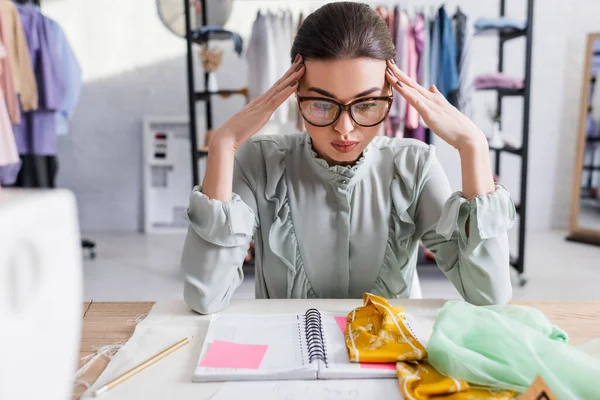 Müde Näherin blickt auf Stoff und Notizbuch auf dem Tisch — Stockfoto