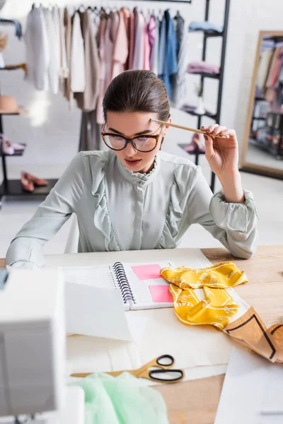 Seamstress holding pencil near fabric, paper and scissors on table — Stock Photo