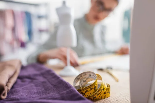 Measuring tape and fabric near blurred seamstress — Stock Photo