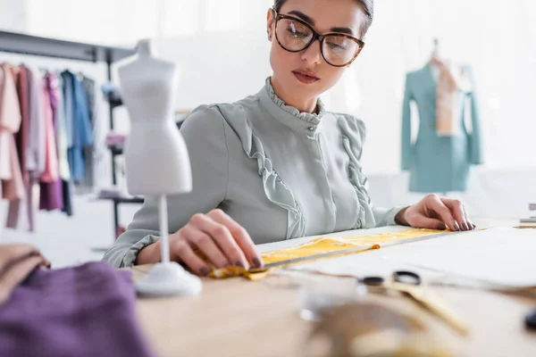 Seamstress holding ruler near fabric and blurred mannequin — Stock Photo