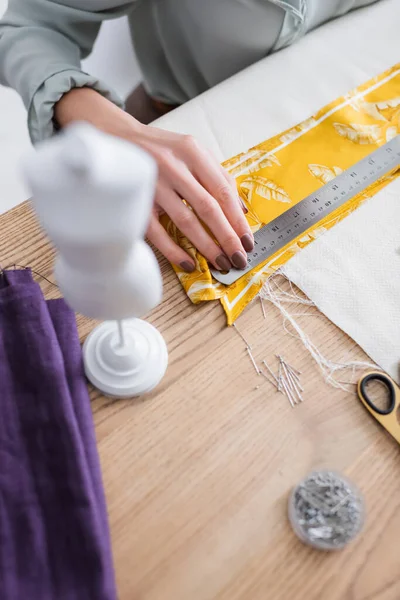 Cropped view of seamstress holding ruler near cloth, scissors and mannequin — Stock Photo