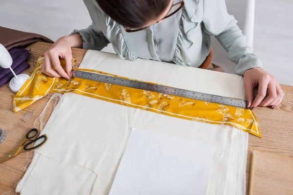 High angle view of designer working with ruler and fabric near scissors on table — Stock Photo