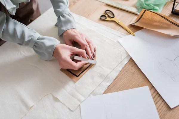 Cropped view of seamstress holding sewing pattern and chalk near sketches — Stock Photo