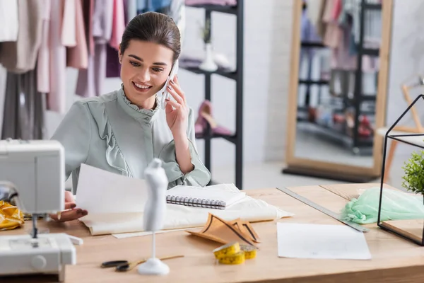 Couturière souriante parlant sur smartphone et tenant un croquis près du tissu — Photo de stock