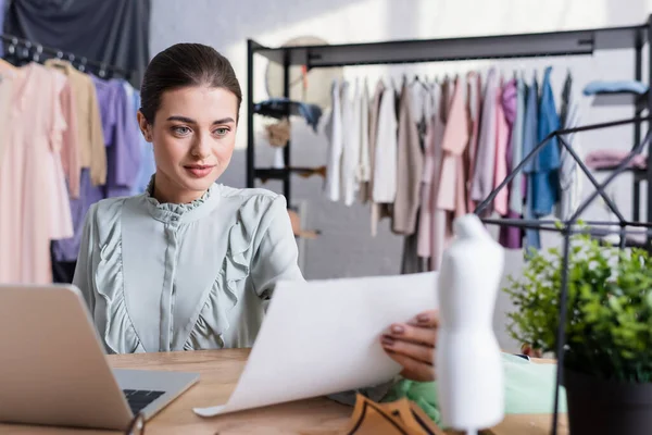 Designer holding paper near blurred laptop and mannequin — Stock Photo
