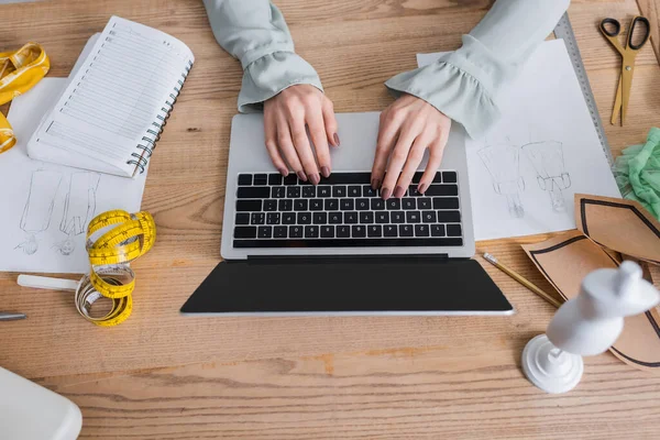 Vista cortada do designer usando laptop perto de esboços e fita métrica na mesa — Fotografia de Stock