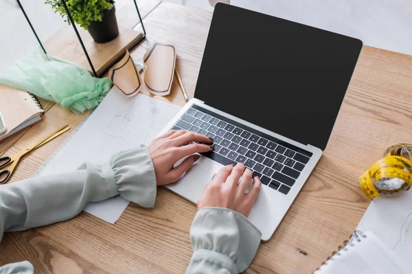 Vista recortada de costurera usando portátil cerca de cinta métrica y bocetos en la mesa - foto de stock