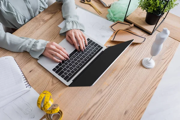 Vista ritagliata del progettista utilizzando laptop vicino schizzi, forbici e modello di cucito sul tavolo — Foto stock