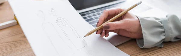 Cropped view of seamstress drawing sketch near blurred laptop, banner — Stock Photo