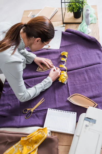 High angle view of designer with sewing pattern marking cloth on table — Stock Photo