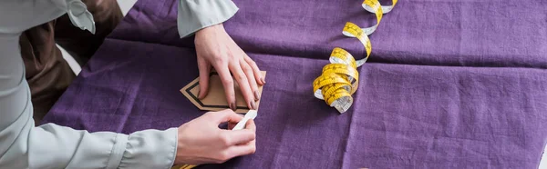 Cropped view of seamstress marking cloth near tape measure, banner — Stock Photo