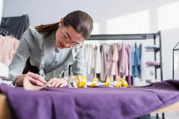 Näherin markiert Stoff in der Nähe von verschwommenem Schnittmuster und Maßband — Stockfoto