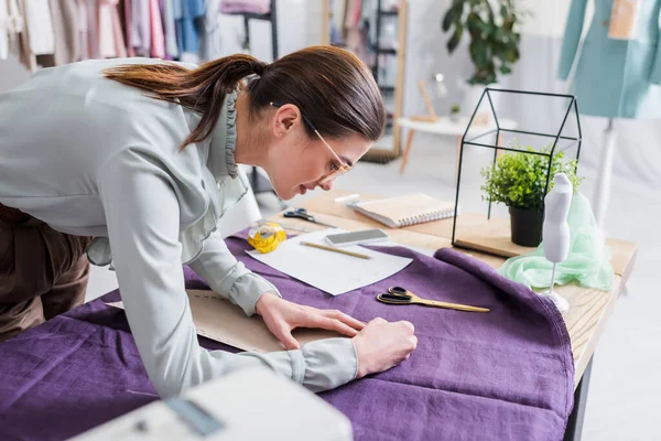 Вид сбоку на улыбающуюся ткань с маркировкой seamstress во время работы с рисунком шитья — стоковое фото