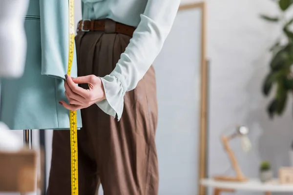 Vista recortada de costurera con cinta métrica cerca de chaqueta borrosa - foto de stock