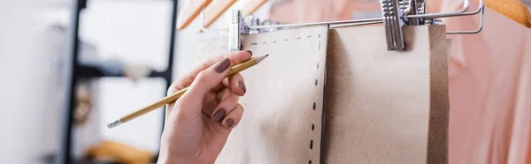 Ausgeschnittene Ansicht des Designers mit Bleistift in der Nähe von Schnittmustern im Atelier, Banner — Stockfoto